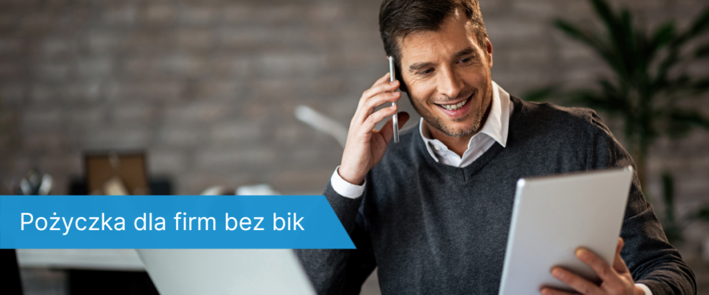 Uśmiechnięty mężczyzna w swetrze, rozmawiający przez telefon i przeglądający tablet w domowym biurze